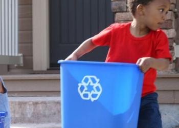 Three children are holding recycle bins and sorting their recyclable materials, outside of their house.